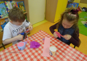 Dwoje dzieci wycinają elementy papierowe do skarbonki.